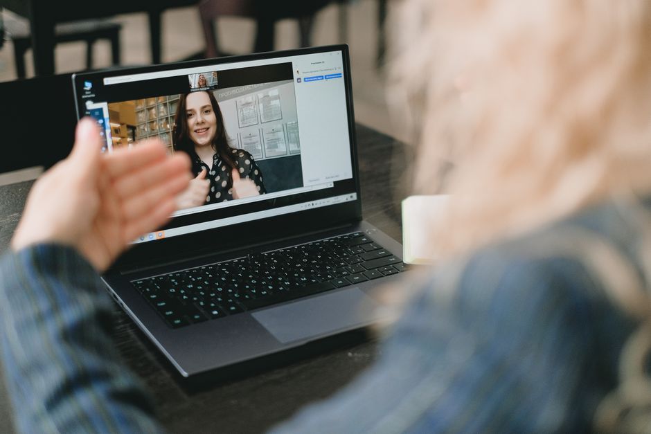 Crop anonymous businesswoman with blond hair in formal clothes sitting at table and having video call via laptop with female colleague during online meeting